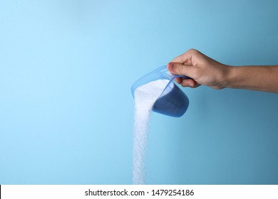 Woman pouring laundry detergent from measuring container against blue background, closeup. Space for text - Shutterstock ID 1479254186