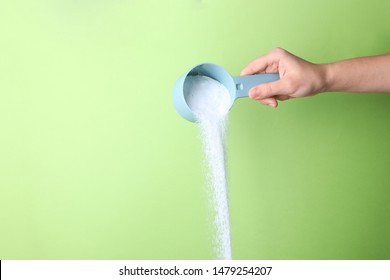 Woman pouring laundry detergent from measuring container against green background, closeup. Space for text - Shutterstock ID 1479254207