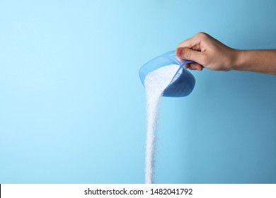 Mujer vertiendo detergente para la ropa desde el recipiente de medida contra fondo azul, cerrar. Espacio para texto