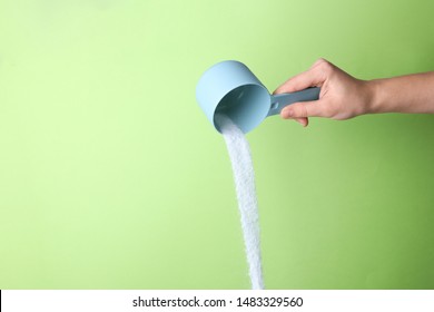 Woman pouring laundry detergent from measuring container against green background, closeup. Space for text - Shutterstock ID 1483329560