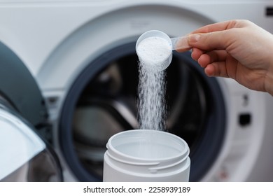 Woman pouring laundry detergent from measuring container against white background, closeup. Woman throws laundry detergent into the washing machine - Shutterstock ID 2258939189