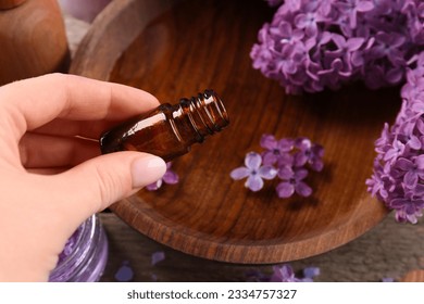 Woman pouring lilac essential oil into bowl at wooden table, closeup - Shutterstock ID 2334757327