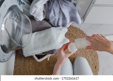 Woman Pouring Liquid Detergent From Bottle For Laundry In Front Of Washer. View From Above