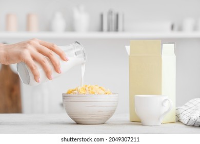 Woman pouring milk from bottle into bowl with corn flakes on table in kitchen - Powered by Shutterstock