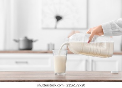 Woman Pouring Milk From Gallon Bottle Into Glass On Table In Kitchen