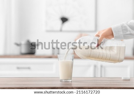 Woman pouring milk from gallon bottle into glass on table in kitchen