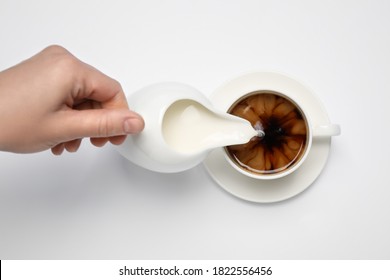 Woman Pouring Milk Into Cup Of Coffee On White Background, Top View