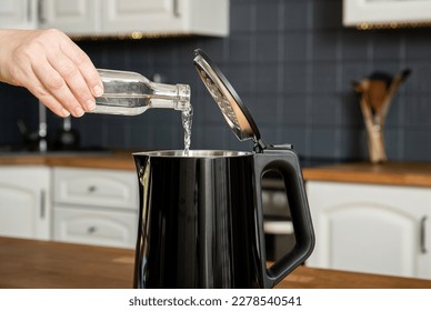 Woman pouring natural destilled acid white vinegar in electric kettle to remove boil away the limescale. Descaling a kettle, remove scale concept. Home kitchen background.