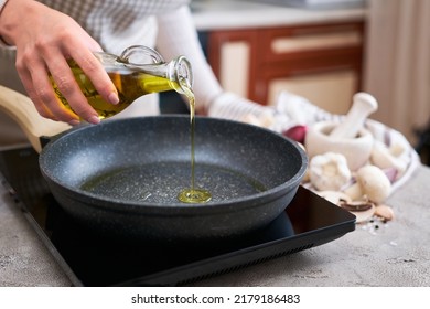 Woman pouring olive oil on frying pan at domestic kitchen