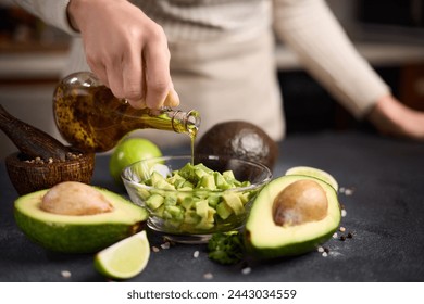 Woman pouring olive oil onto Chopped avocado in glass bowl and avocado Halves - Powered by Shutterstock