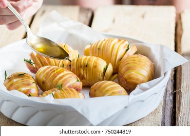 Woman pouring olive oil over a ceramic tray with fan-shaped potatoes  - Powered by Shutterstock