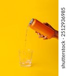 Woman pouring an orange drink from an aluminum can into a glass with ice on a yellow background