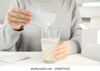 Woman pouring powder from medicine sachet into glass with water at table, closeup