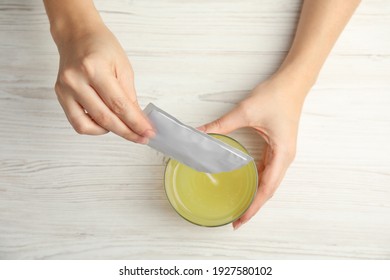 Woman Pouring Powder From Medicine Sachet Into Glass With Water At Table, Top View