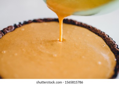 Woman Pouring Pumpkin Custard Into Pie Crust