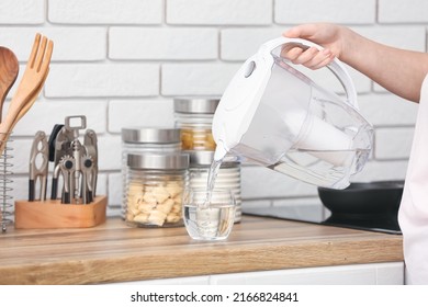Woman pouring purified water into glass from filter jug in kitchen