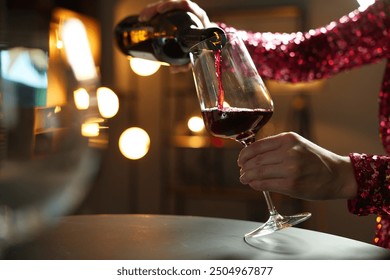 Woman pouring red wine from bottle into glass at table indoors, closeup - Powered by Shutterstock