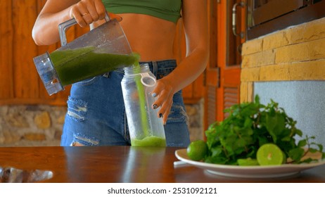 Woman pouring refreshing green smoothie into glass with ice, accompanied by fresh mint and lime slices on table. Woman is pouring green smoothie from bottle into glass with ice. Healthy eating - Powered by Shutterstock