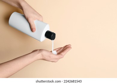 Woman pouring shampoo into palm on beige background, top view. Space for text