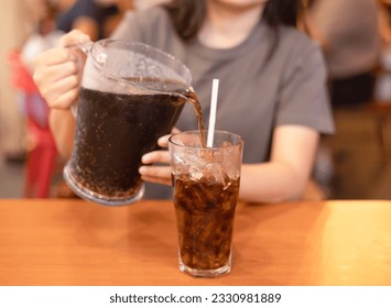 Woman pouring soft drink into glass in the restaurant. close-up the stream of cola is poured into a glass with ice on a dark. sugary drinks, Unhealthy diet, sweet sugary soft drinks, coke concept.