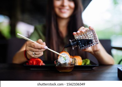 Woman pouring soy sauce on sushi roll. Sticks of sushi soy sauce. Leisure and Food