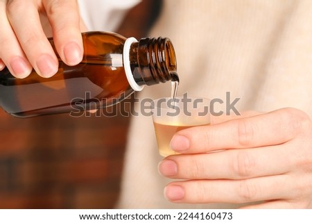 Woman pouring syrup from bottle into measuring cup, closeup. Cold medicine