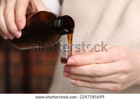 Woman pouring syrup from bottle into measuring cup, closeup. Cold medicine