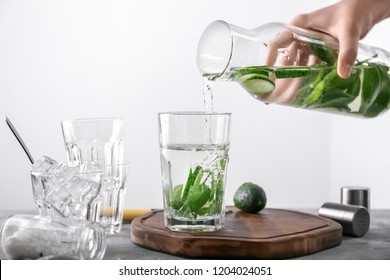 Woman Pouring Tasty Fresh Cucumber Water From Bottle Into Glass On Light Background