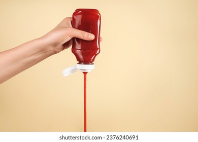 Woman pouring tasty ketchup from bottle on beige background, closeup. Space for text