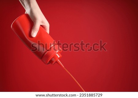 Woman pouring tasty ketchup from bottle on red background, closeup. Space for text