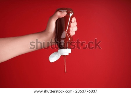 Woman pouring tasty ketchup from bottle on red background, closeup