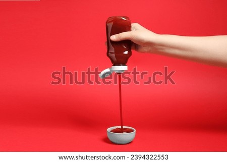 Woman pouring tasty ketchup from bottle into bowl on red background, closeup
