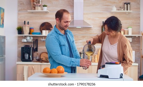 Woman Pouring Tasty Smoothie From Blender In Glasses For Her And Husband. Cheerful Family Making Together Organic Healthy Fresh Nutritious Tasty Juice For Breakfast From Fresh Fruits While On A Diet.