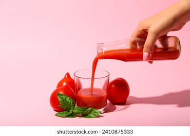Woman pouring tasty tomato juice from bottle into glass on pink background