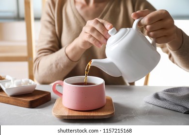 Woman pouring tea into ceramic cup at table, closeup
