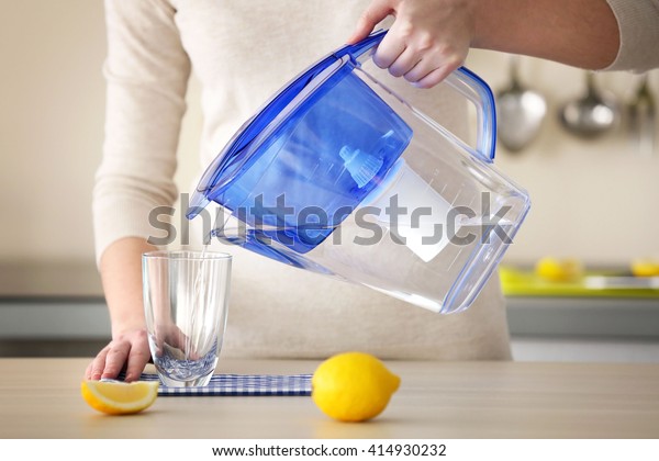 Woman pouring water from filter jug into glass in\
the kitchen