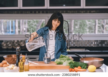 Woman pouring water in her kitchen. Imagine de stoc © 