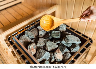 Woman is pouring water into hot stone in Sauna spa room