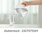 Woman pouring water from jug into glass at white table indoors, closeup