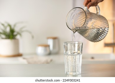 Woman pouring water from jug into glass at white table in kitchen, closeup. Space for text - Shutterstock ID 2249303241