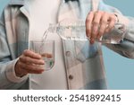 Woman pouring water with plastic into glass on blue background, closeup. Microplastic Awareness Month