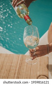 Woman Pouring White Wine Into A Glass By The Pool On A Sunny Summer Day.