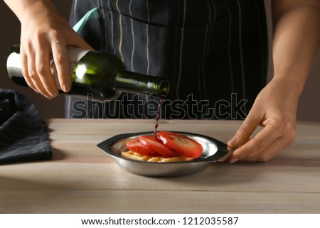 Woman pouring wine onto plate with sweet waffle and stewed pear in kitchen