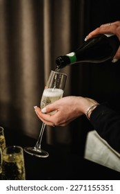 Woman pours champagne into a flute glass. Champaign is being pored into glasses. Waiter pouring white sparkling wine. Bottle in a closeup view. Catering service concept.