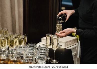 Woman pours champagne into flute glasses. Champaign is being pored into glasses. The waiter pouring white sparkling wine. Bottle in a closeup view. Rows of full glasses. Catering service concept.