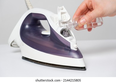 A Woman Pours A Cleansing Liquid Into A Water Tank In An Iron. Cleaning The Iron From Scale