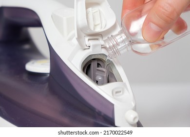 A Woman Pours A Cleansing Liquid Into A Water Tank In An Iron. Cleaning The Iron From Scale