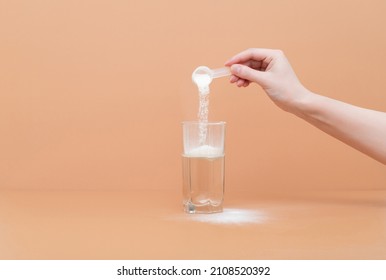 Woman pours collagen powder or protein in a glass of water on a beige background. A healthy and anti aging supplement. Copy space