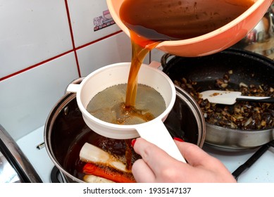 The woman pours the decoction of the mushroom soup through a plastic strainer. - Shutterstock ID 1935147137
