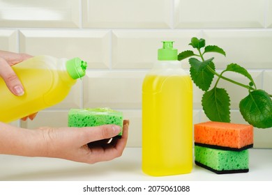Woman pours dish detergent onto a sponge. Detergent bottle for dishes with mint and orange. Luminous aroma. spring-cleaning. Housewife uses dishwashing detergent for wash up dishes in the kitchen